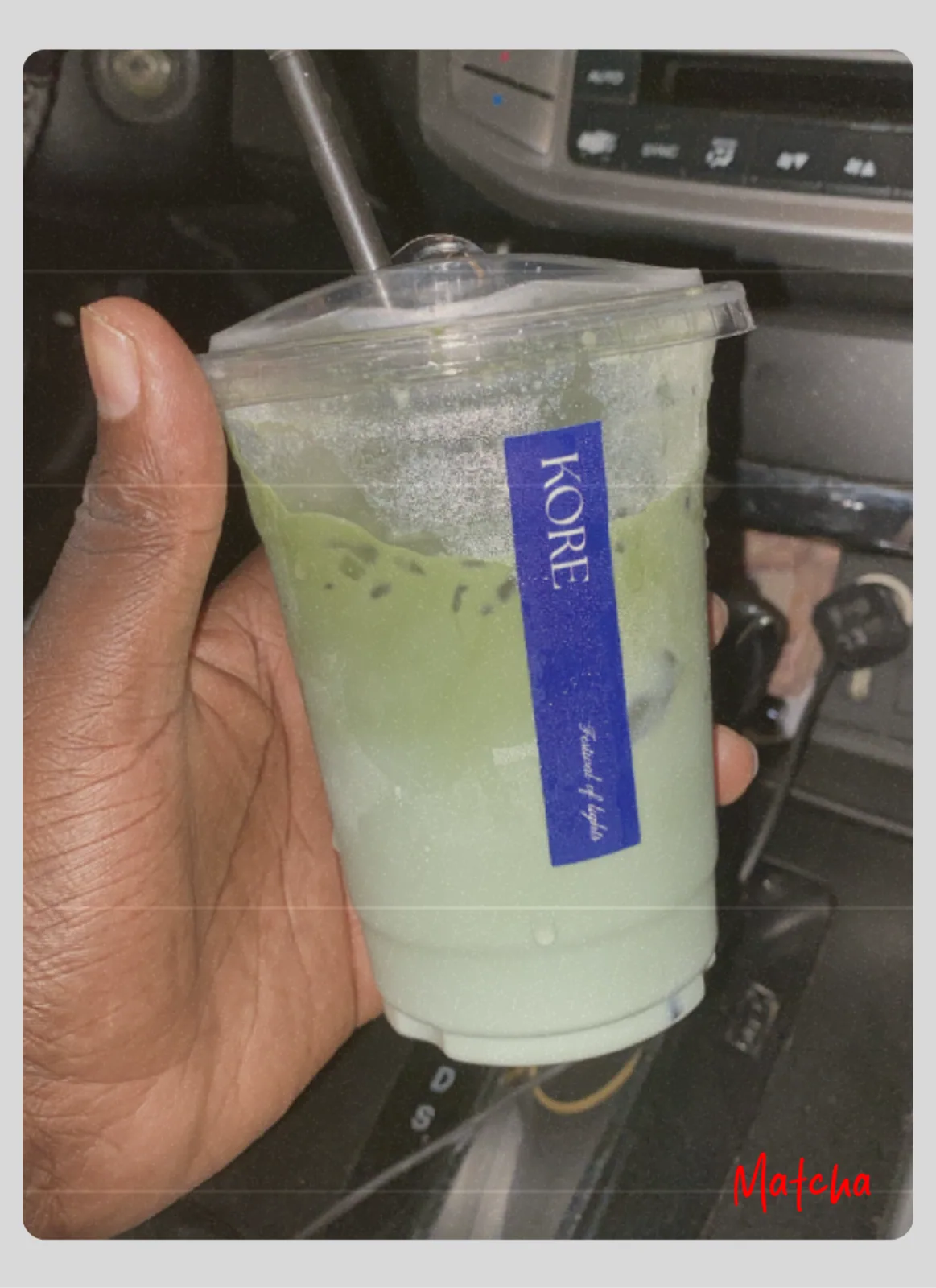 A hand holding an iced matcha drink inside a car