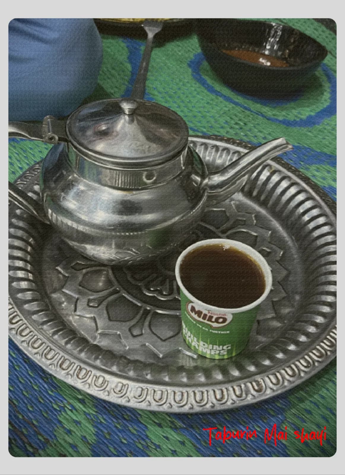 A metal teapot and a cup of tea on an engraved serving tray